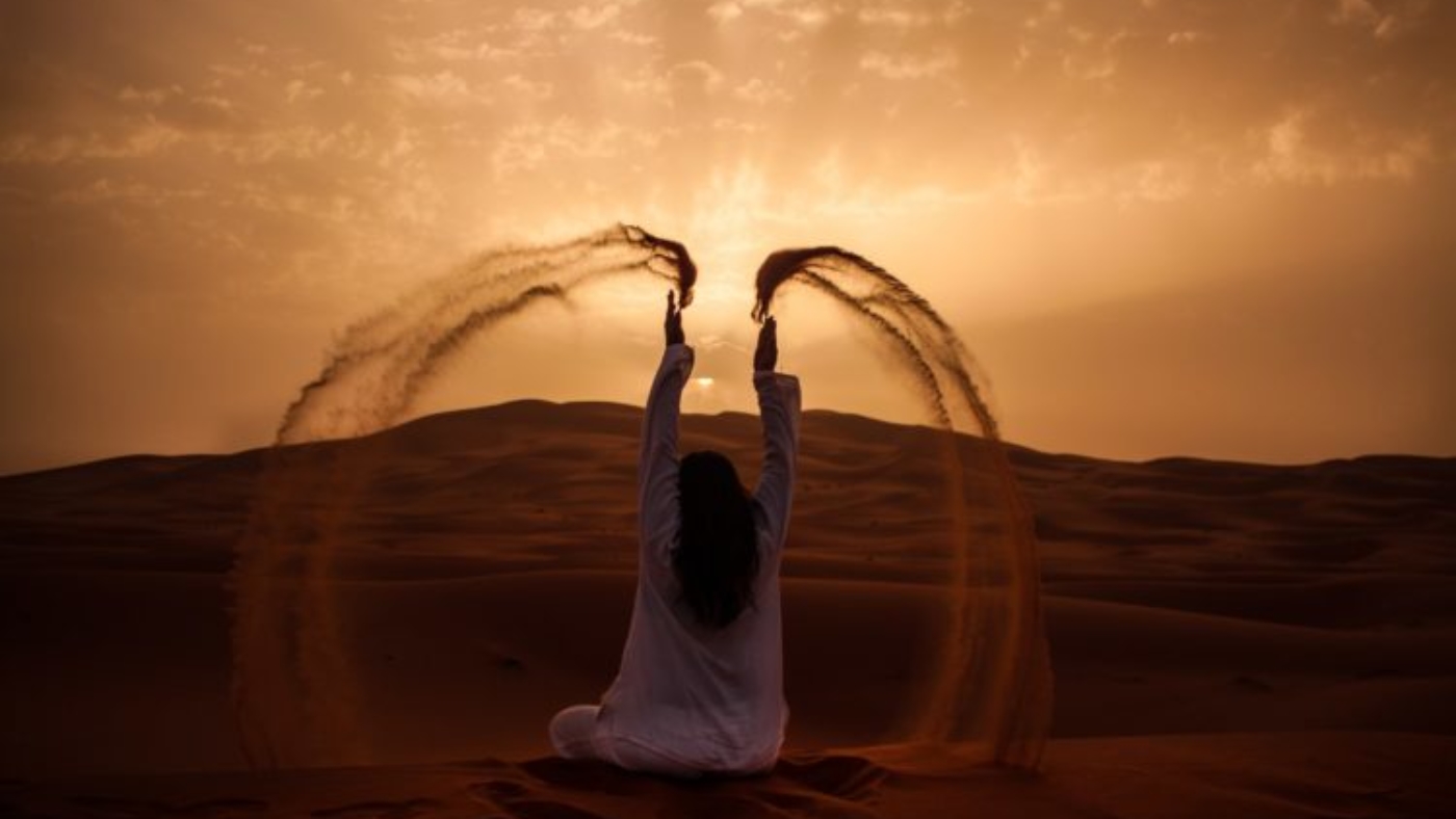 Woman sitting in desert with sunset